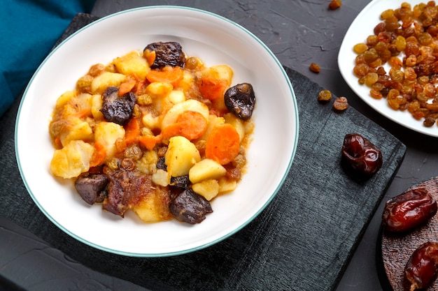 Plat de cuisine juive douce zimmes avec dattes végétariennes carottes dans une assiette sur une surface en béton sur un tableau noir