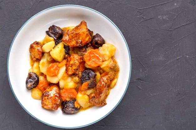 Un plat de cuisine juive tsimes sucrés avec des carottes, des dattes et de la viande de dinde dans une assiette blanche sur une surface en béton