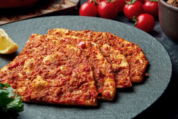 Plat de cuisine turque - pide avec de la viande hachée et des tomates sur une plaque noire. Turc lahmajun, gros plan,