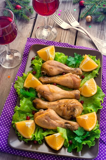 Plat avec des cuisses de poulet rôties, des légumes verts, des oranges et du vin.