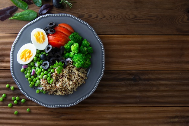 Plat de désintoxication en bonne santé avec oeuf, pois verts, quinoa, tomate et brocoli, fond en bois.