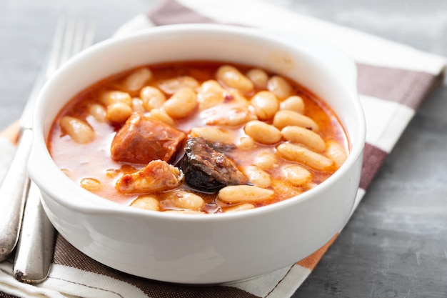 Plat espagnol typique fabada, haricots avec saucisses fumées et viande sur bol blanc