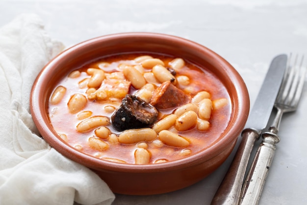 Plat espagnol typique fabada, haricots avec saucisses fumées et viande sur plat en céramique marron