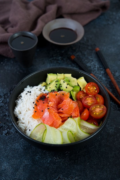 Un plat hawaïen populaire, Poke dans une assiette de poisson rouge, de riz et de légumes. Plaque Poke sur un fond de béton noir