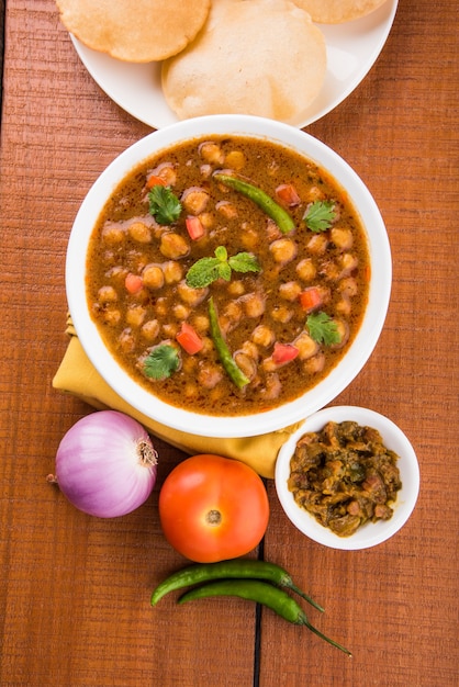 Plat Indien Au Curry De Pois Chiches épicé, également Connu Sous Le Nom De Chola Ou Chana Masala Ou Communément Chole, Servi Avec Des Puri Frits Ou Des Poori Sur Fond Coloré Ou En Bois. Mise Au Point Sélective