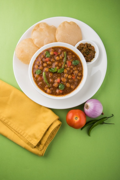 Plat indien au curry de pois chiches épicé, également connu sous le nom de Chola ou Chana Masala ou communément Chole, servi avec des puri frits ou des poori sur fond coloré ou en bois. Mise au point sélective