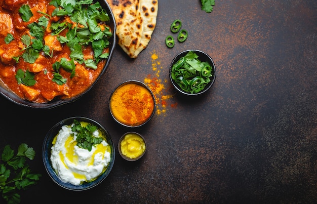 Plat indien authentique Poulet tikka masala avec un espace pour le texte. Viande épicée au curry dans un bol avec du pain frais naan, sauce raita au yaourt sur fond sombre rustique, vue de dessus, gros plan, espace pour copie