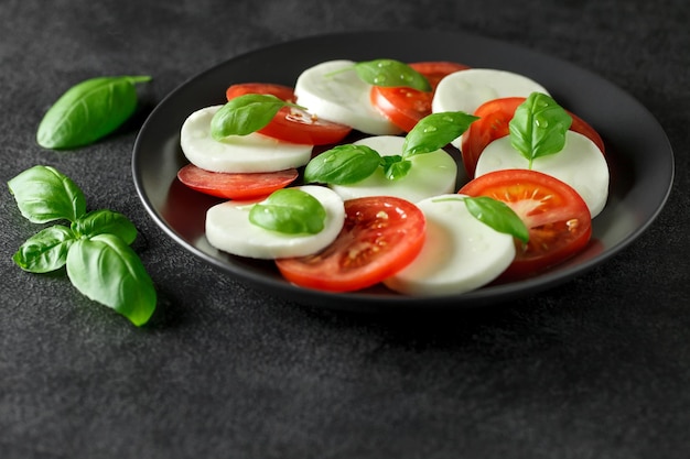 Plat italien Caprese de tomates mozzarella et basilic sur plaque sombre mise au point sélective