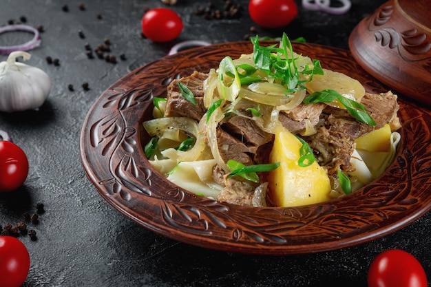 Plat kazakh traditionnel beshbarmak avec oignons à pâte bouillie et mouton et boeuf dans un pot en argile