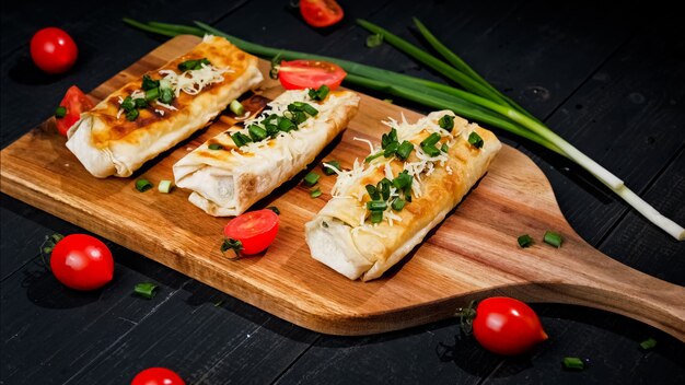 Le plat mexicain de gâteau plat de maïs Tako avec garniture de légumes sur une planche de bois sur fond noir