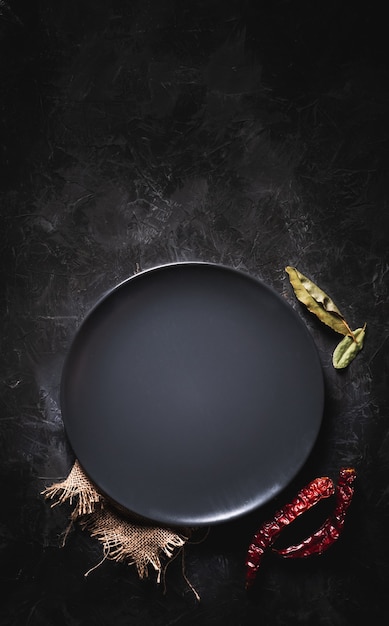 Plat noir rond vide sur une table sombre avec quelques ingrédients pour la cuisson