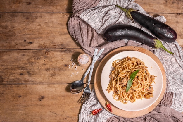 Plat de pâtes traditionnelles siciliennes d'aubergines sautées garnies de sauce tomate. Nourriture servie sur une assiette en céramique, cuisine italienne, lumière dure moderne, ombre sombre. Fond de table en bois, vue de dessus
