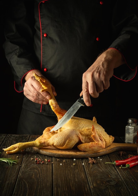 Un plat de poulet frit par les mains du chef dans la cuisine du restaurant Avant la cuisson, le gril doit être coupé sur une planche à découper Couteau dans la main du cuisinier