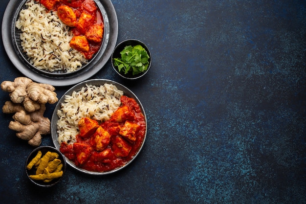 Plat de poulet tikka masala avec riz, pain indien plat et épices dans des plaques de métal rustiques sur fond de béton vue de dessus. Curry de poulet aux tomates, repas indien traditionnel, espace libre pour le texte