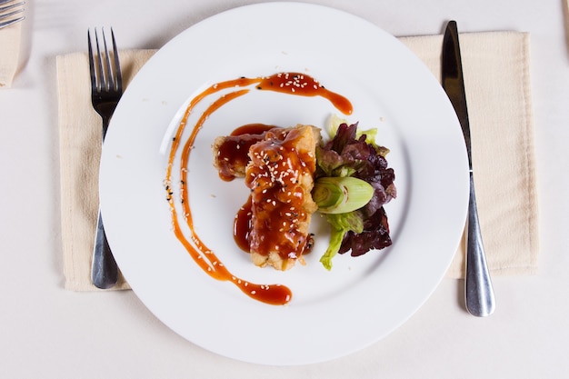 Plat principal savoureux gastronomique sur une assiette ronde blanche avec des ustensiles sur les côtés servis sur une table blanche pour l'invité du restaurant.