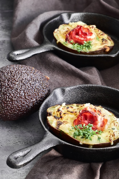 Plat de régime céto: bateaux d'avocat avec bacon croquant, fromage fondu et pousses de cresson sur dark