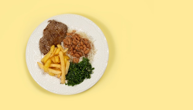 Plat avec riz, haricots, steak, frites et chou braisé dans une assiette blanche sur fond jaune