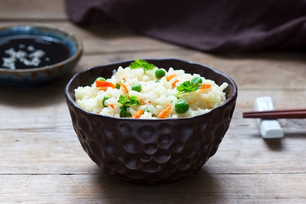 Plat de riz végétarien avec légumes et pois verts sur une surface en bois