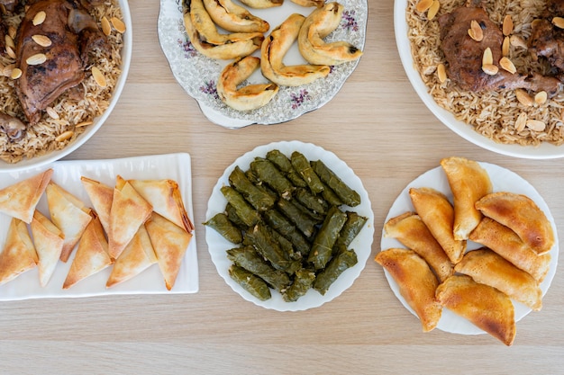 Un plat de rouleaux de raisin sur une table en bois vu d'en haut avec du sambousek et du qatayef