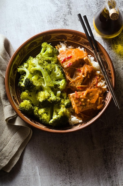 Photo plat de saumon thaï dans une sauce à la noix de coco avec du brocoli frais et du riz dans un bol en argile avec des baguettes des aliments sains avec de la vitamine b5