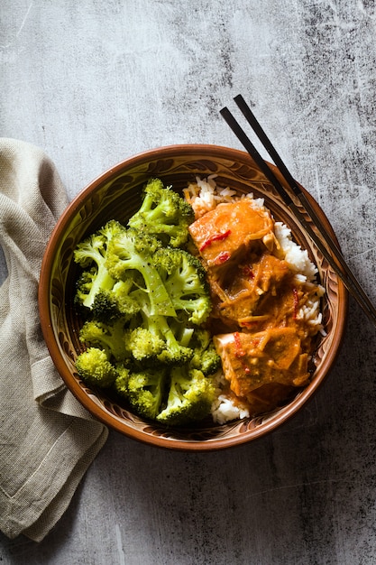 Plat de saumon thaï à la noix de coco avec brocoli frais et riz dans un bol en argile avec des baguettes