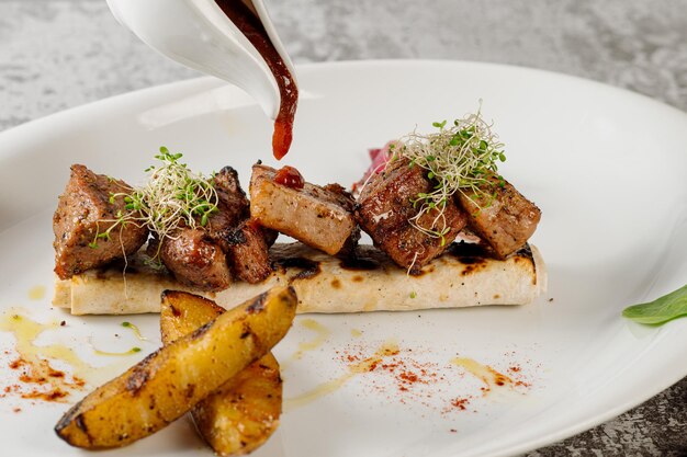 Plat de savoureuse viande de barbecue grillée avec pommes de terre et herbes sur fond de béton gris