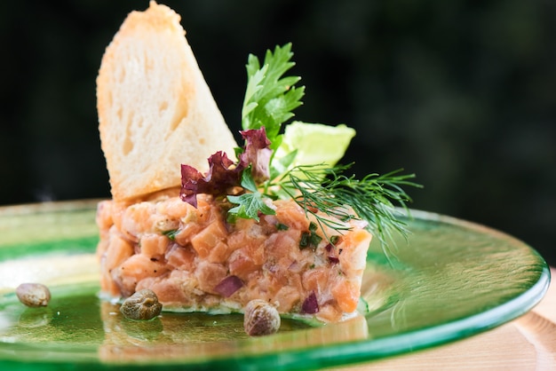 Un plat de tartare de saumon, oignons rouges et verts, zeste de citron et huile d'olive servi dans une assiette