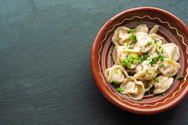 un plat traditionnel classique de boulettes de pelmeni avec de la viande, du beurre, du poivre et des légumes verts, de la nourriture