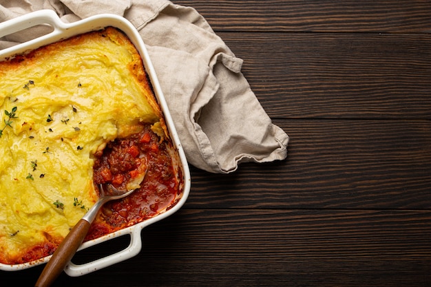 Plat traditionnel de la cuisine britannique Casserole de tarte au berger avec viande hachée et purée de pommes de terre dans un plat de cuisson en céramique sur une table rustique en bois marron avec une cuillère d'en haut avec un espace pour le texte