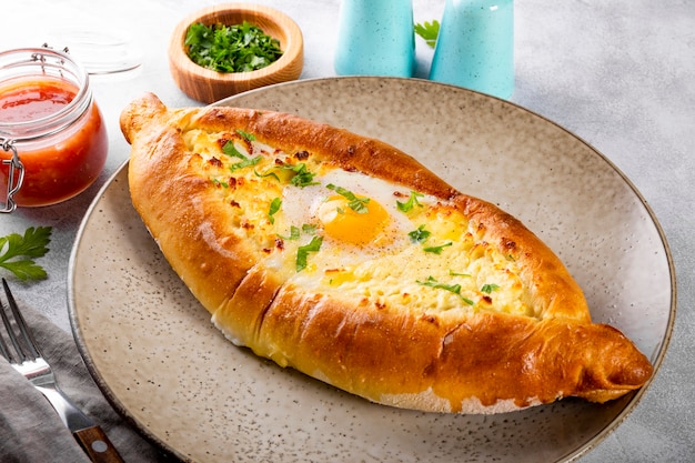 Un plat traditionnel de la cuisine géorgienne khachapuri adjare avec fromage et œuf et tomate épicée