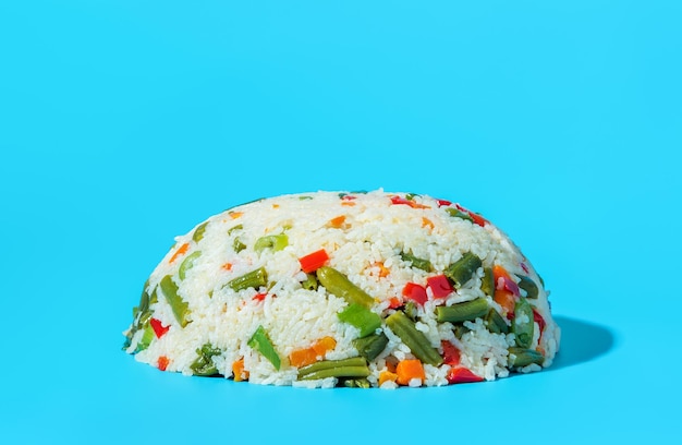 Plat végétalien riz blanc avec un mélange de légumes isolé sur fond bleu