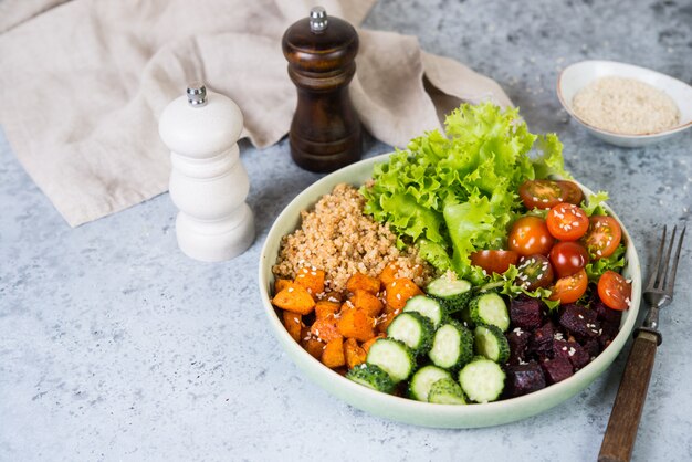 Plat végétarien un bol de quinoa sain avec des légumes frais et cuits au four sur un fond de béton gris.