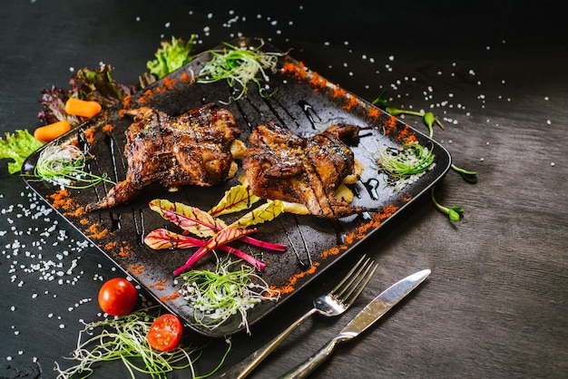 Un plat avec de la viande de caille rôtie avec des légumes sur fond noir