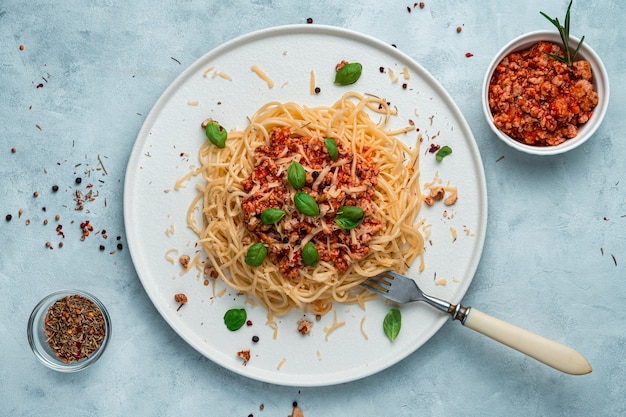 Un plat de viande hachée, spaghetti et sauce tomate sur fond gris-bleu.