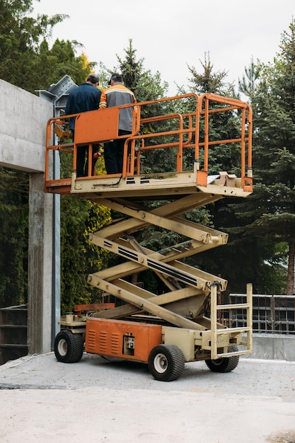 Plate-forme d'ascenseur à ciseaux avec des travailleurs sur un chantier de construction construisant une maison en béton avec mobile