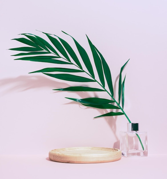 Une plate-forme ronde en bois pour présenter des produits cosmétiques et un vase en verre avec une feuille de palmier verte