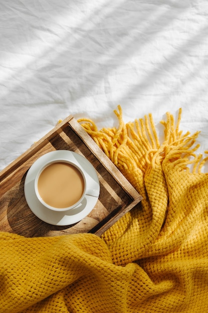 Plateau en bois avec café et plaid chaud sur literie blanche. Petit déjeuner au lit. Concept d'hygiène.