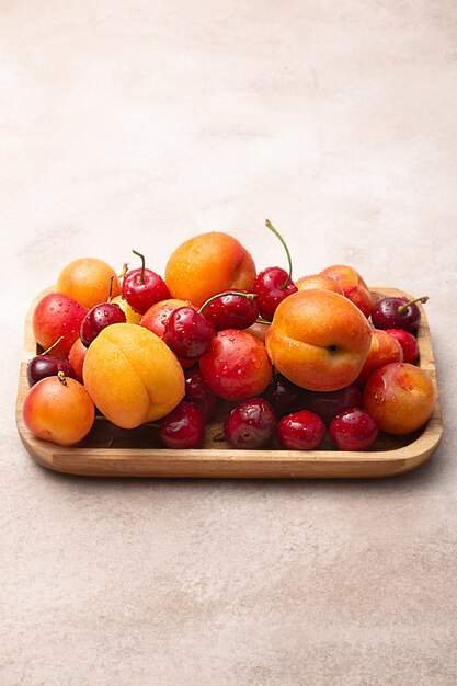 Plateau en bois avec cerises fraîches, prunes et abricots