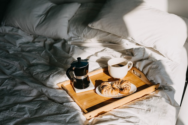 un plateau en bois avec des croissants et une tasse de café sur le lit
