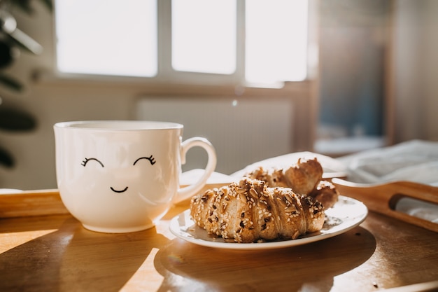 un plateau en bois avec des croissants et une tasse de café sur le lit