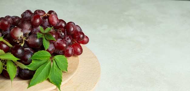 Plateau en bois avec du raisin sur fond texturé blanc