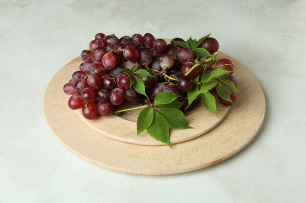 Plateau en bois avec du raisin sur fond texturé blanc