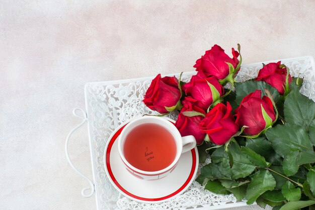 sur un plateau un bouquet de roses rouges et une tasse de thé