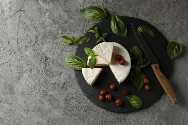 Plateau avec camembert, noisette, basilic et couteau sur fond gris