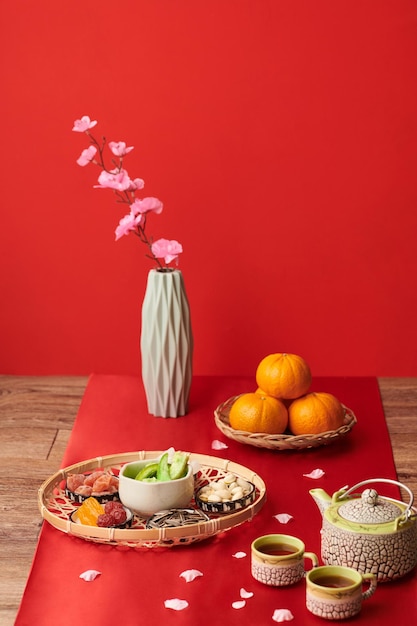 Plateau avec des collations traditionnelles du tet et des mandarines mûres sur une table recouverte de tissu rouge