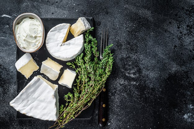 Plateau à fromage. Camembert, Brie, Gorgonzola et fromage à la crème bleu au thym. Fond noir. Vue de dessus. Espace de copie.