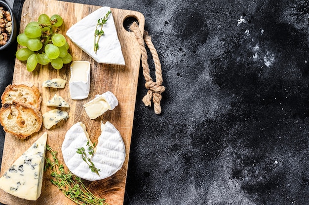 Plateau de fromages avec camembert français, brie et fromage bleu, raisins et noix. Fond noir. Vue de dessus. Copiez l'espace.