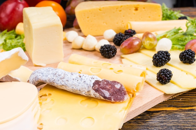 Plateau de fromages gastronomiques avec variété de fromages, saucisses de viande séchée et fruits frais servis sur une table en bois rustique avec grain de bois