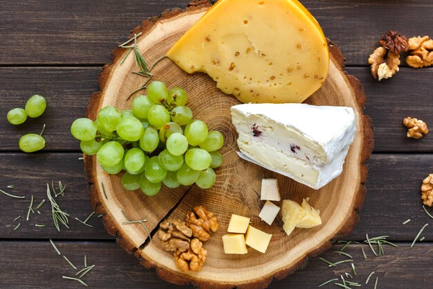 Plateau de fromages, herbe de gouda et roquefort bleu sur planche de bois avec raisins et noix, nature morte. Vue de dessus