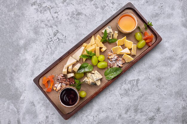 Plateau de fromages sur une planche de bois avec raisins, menthe, miel et confiture, vue du dessus